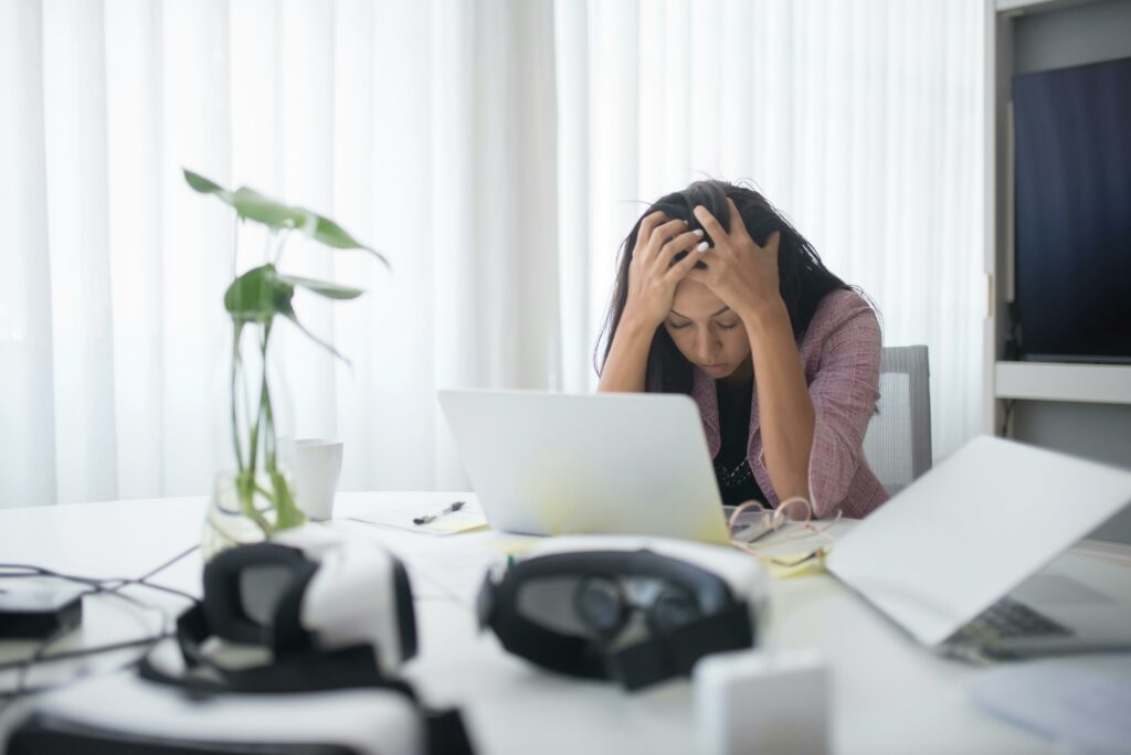 Frustrated woman sitting at desk with laptop, showing stress in a modern office environment.