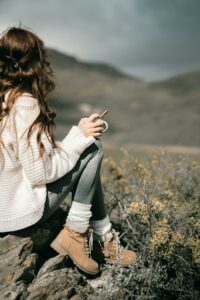 Woman in a white sweater sitting on rocks, enjoying a scenic mountain view.